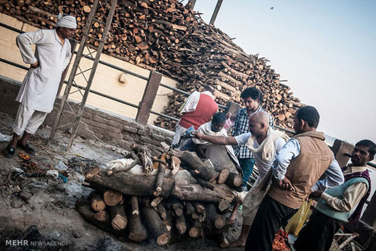آماده سازی یک مرده برای سوزاندن  از طریق افشاندن روغن و... در حضور خانواده متوفی در هند  همچنین خروارها چوب برای سوزاندن مردگان که در این مکان دپو شده است
